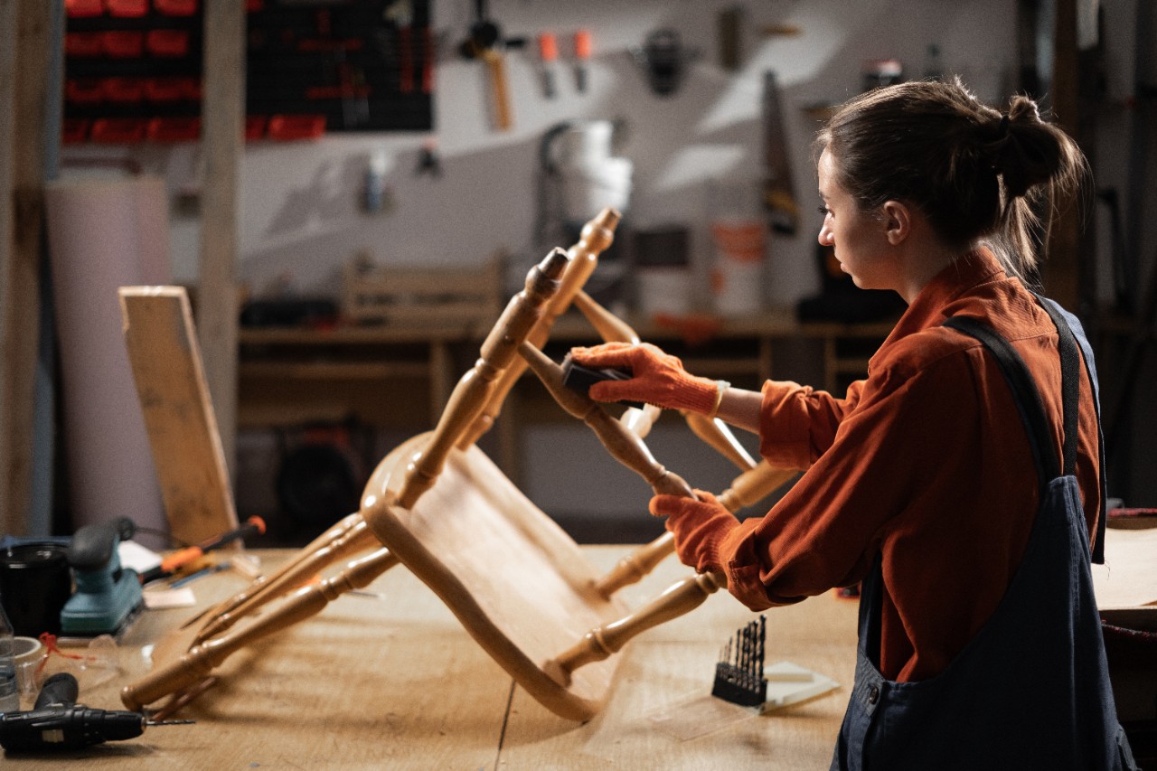 woman restoring furniture sanding old wooden chair in workshop with dark light. Copy space